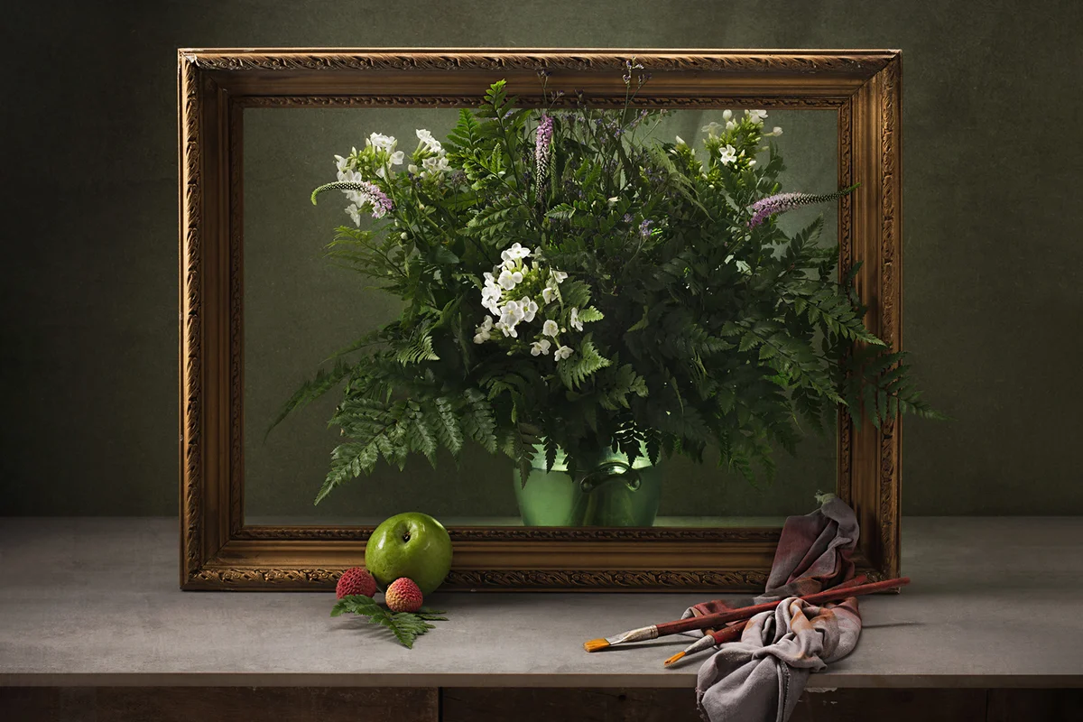 Plant inside of picture frame on table with paintbrushes