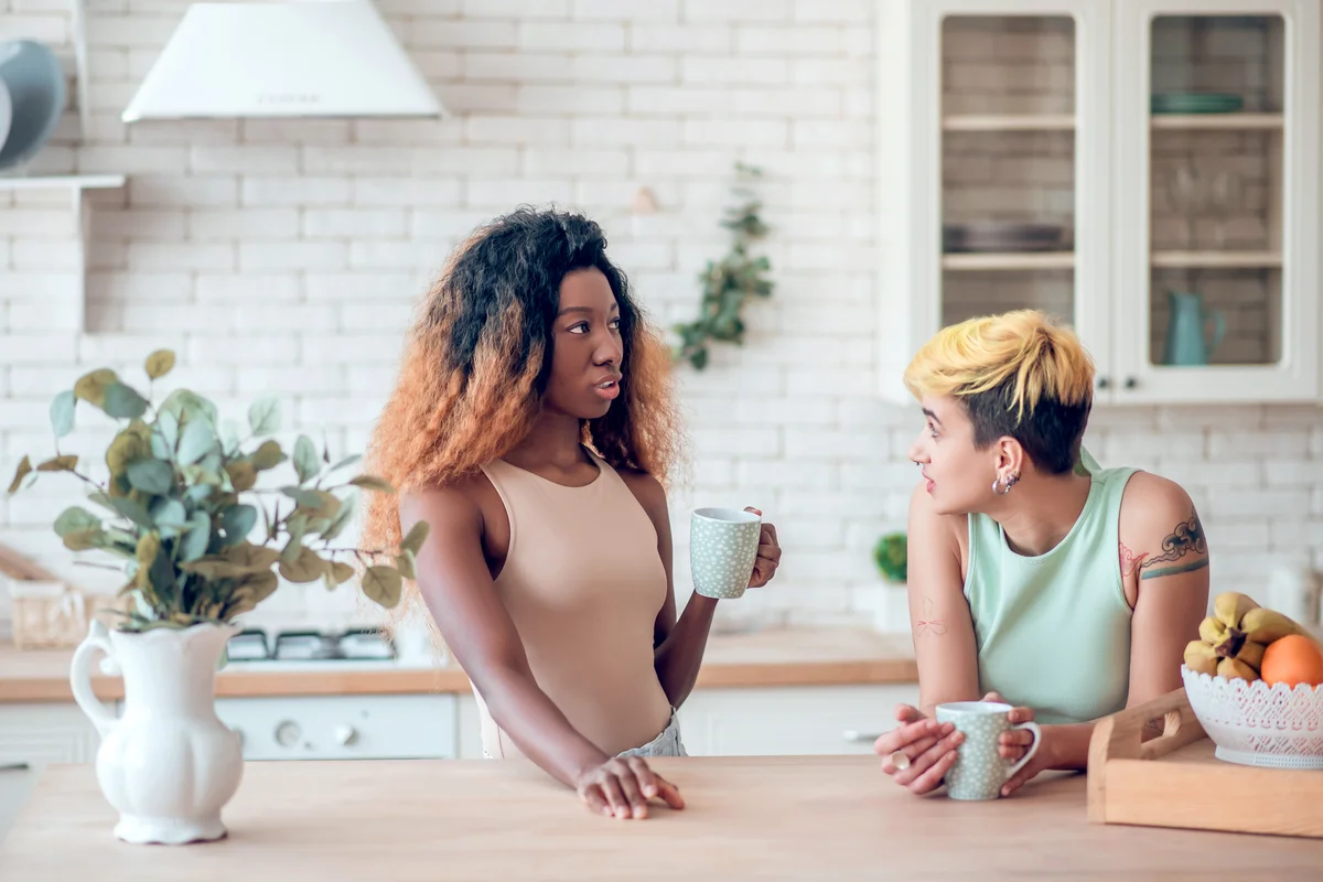Girlfriends drinking coffee in kitchen at home and talking about serious things