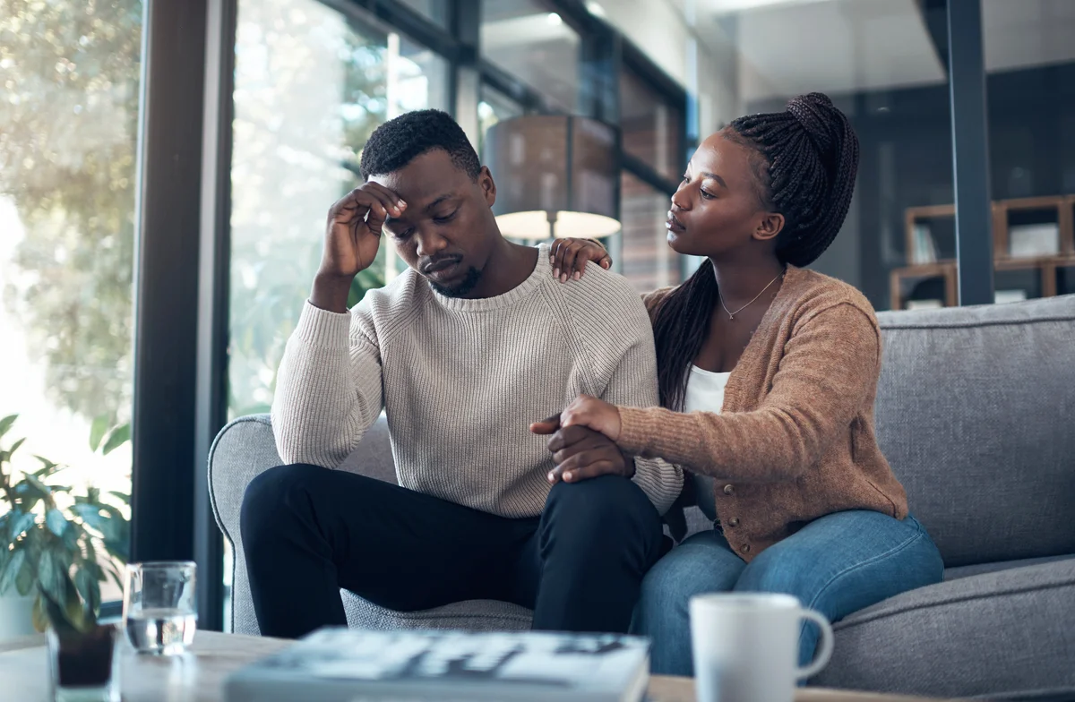 Young man sitting in his living room and stressing while his girlfriend comforts him