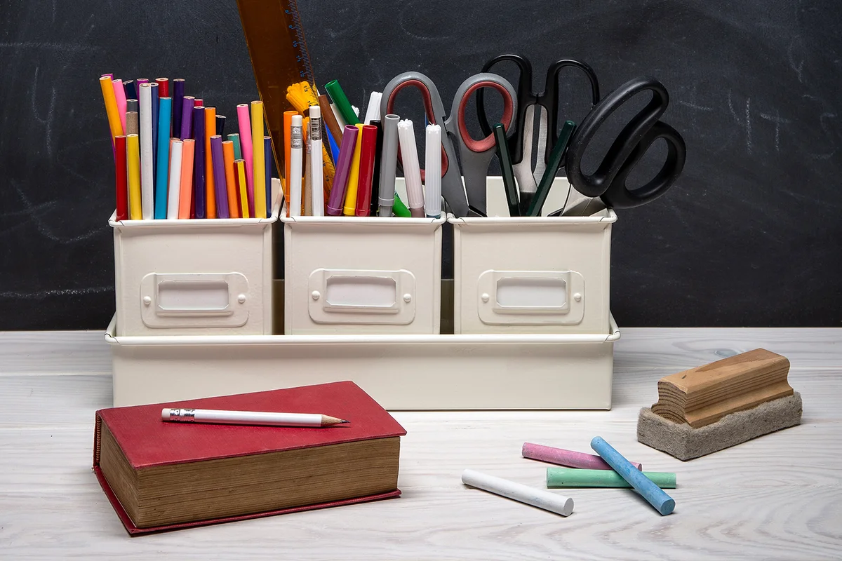 Close-up of school supplies on table against blackboard