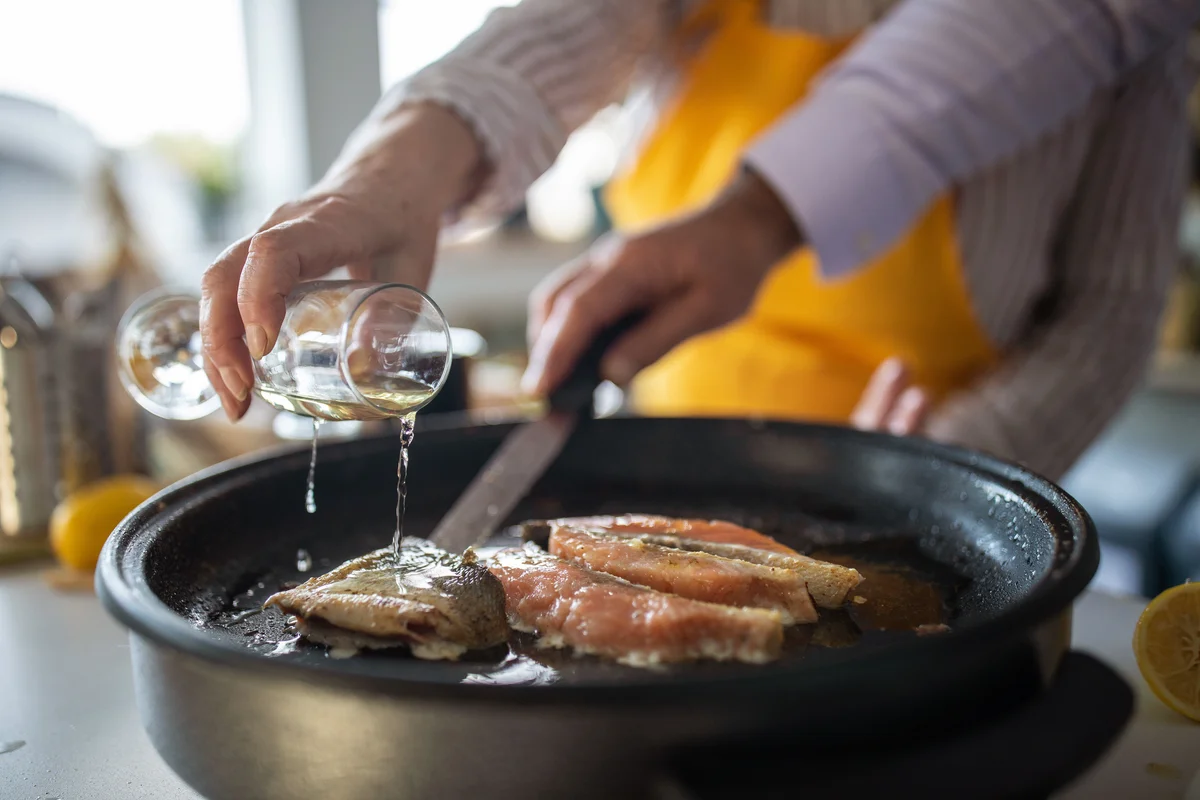 Woman adding white wine while preparing fish