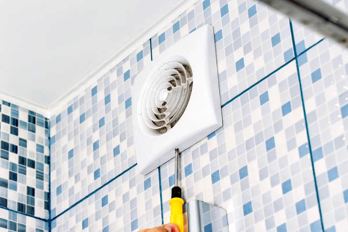 Man removes the ventilation grill in the bathroom with a screwdriver