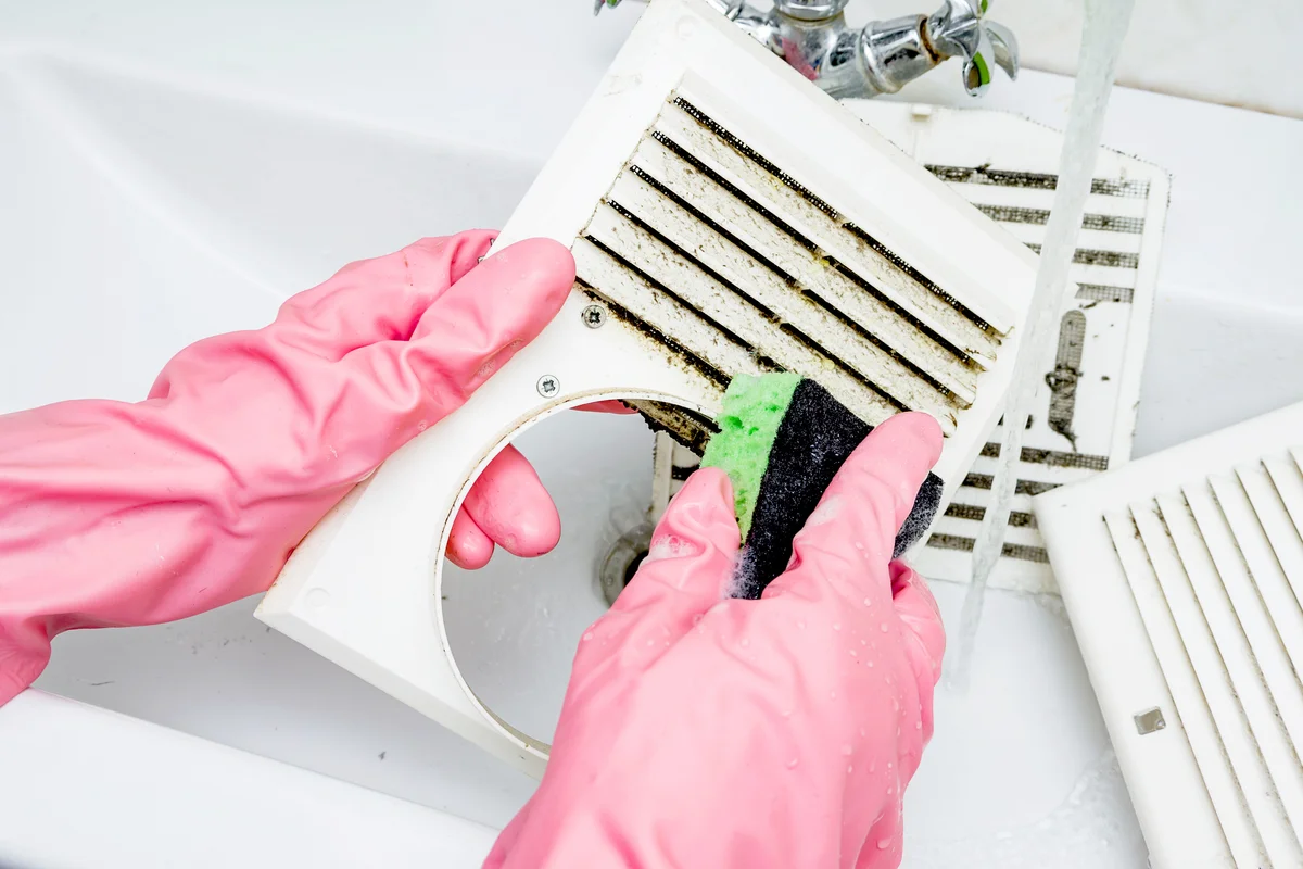 Woman washes with a sponge and soap suds grill of the ventilation return duct blocked by dust and debris
