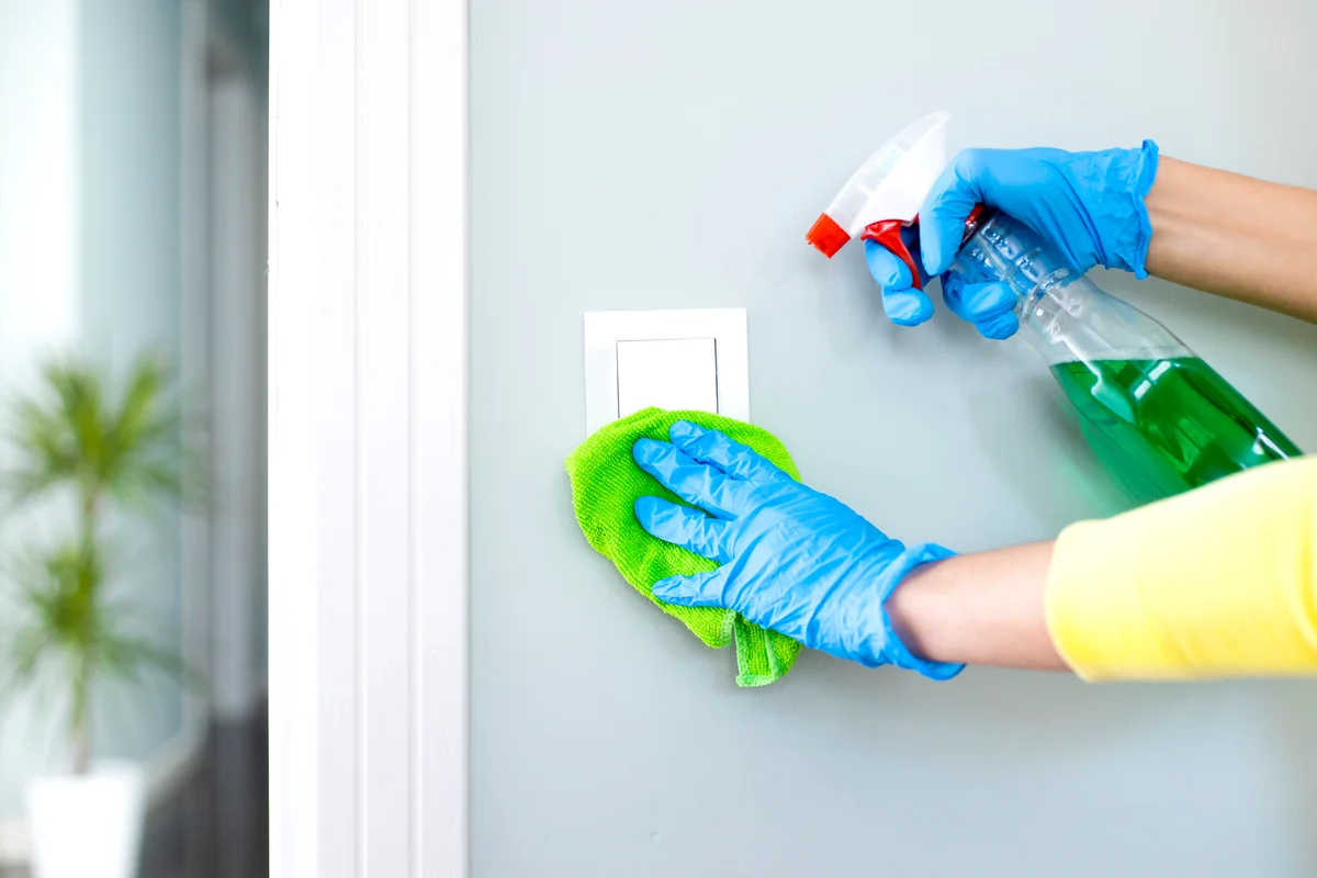 Woman cleaning a light switch with a disinfecting spray