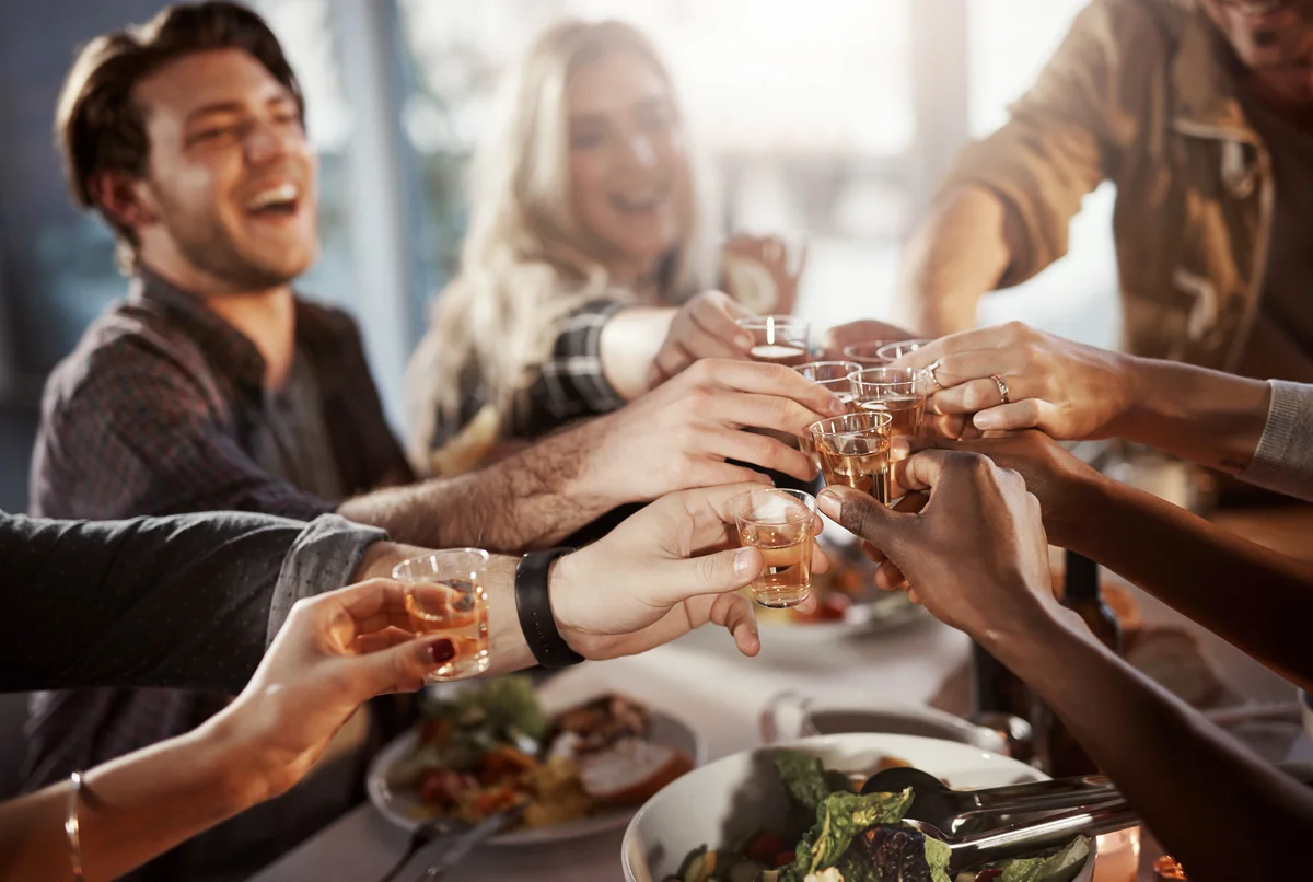 Group of young friends making a toast with shots at a dinner party