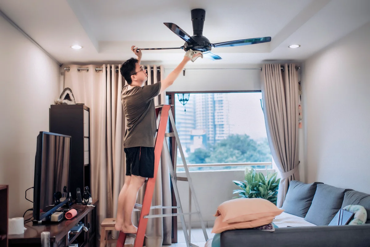 Man cleaning ceiling fan at home