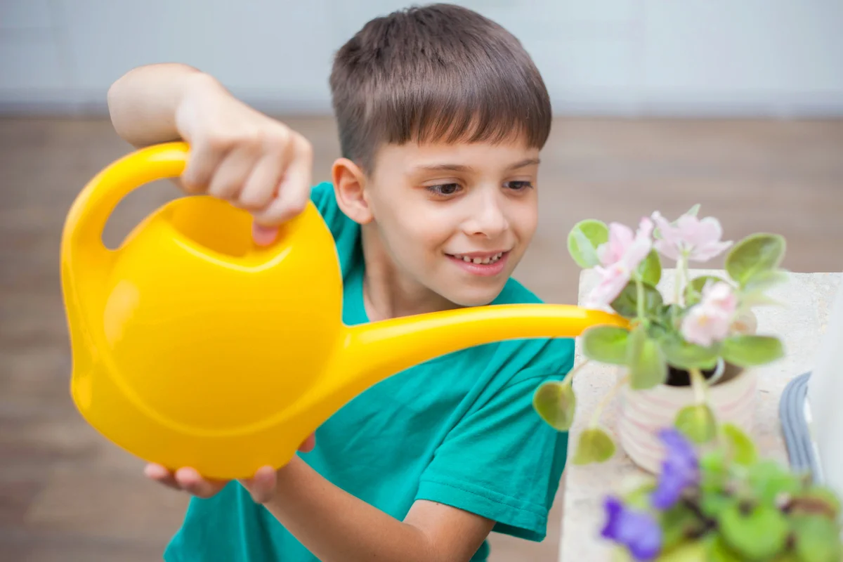 Cute boy watering blooming house plants with watering can