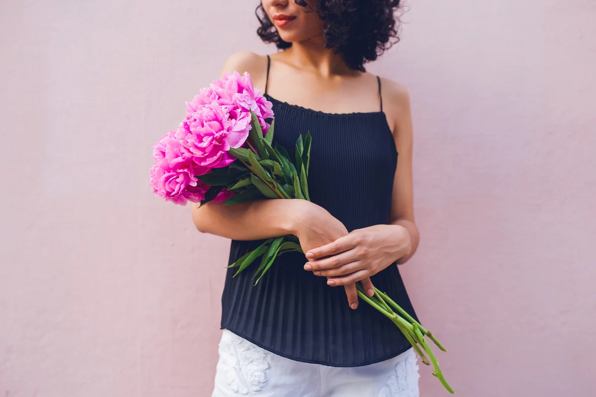 Woman holding a bouquet while posing against a pink background wall