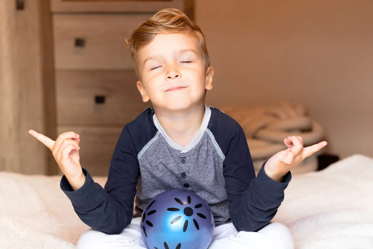 Small Boy Practicing Yoga And Meditating With Eyes Closed On A Bed