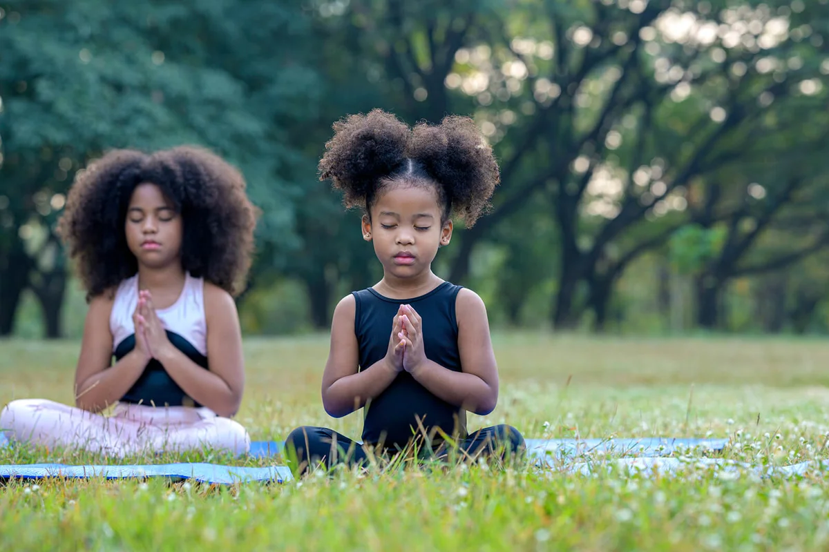 cute children in sportware is meditating on yoga mat outdoor