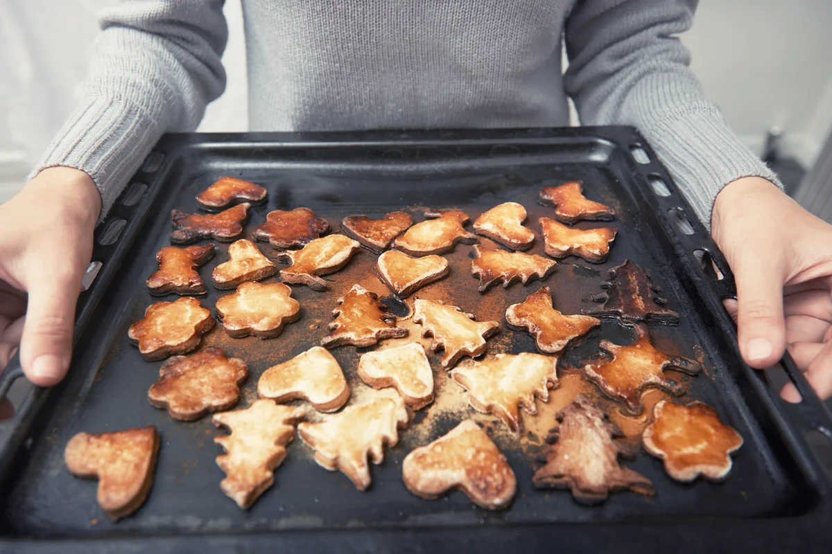 Woman hands holding baking tray with burned cookies