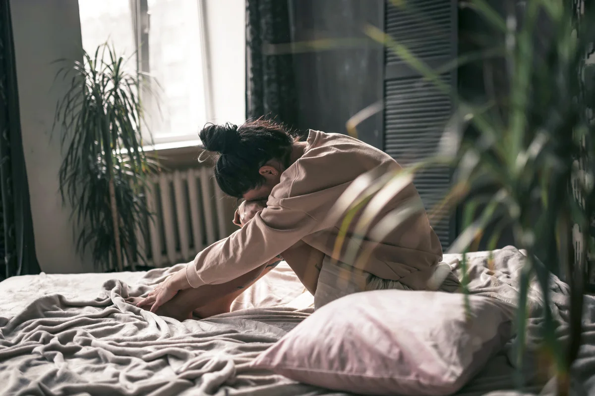 Sad young woman sitting on bed