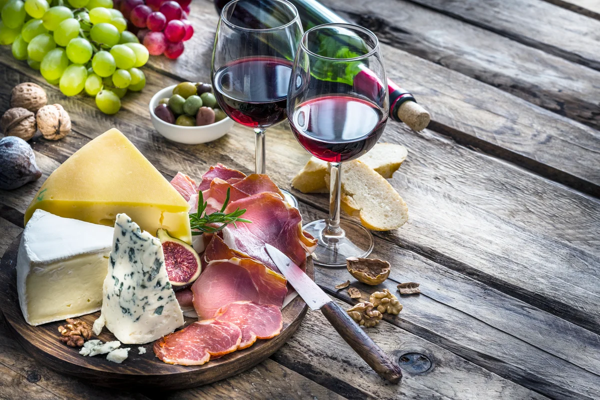 Appetizer: red wine, cheese and cured ham on rustic wooden table