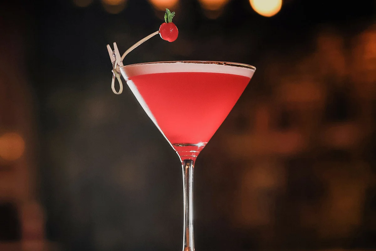 Red alcoholic cocktail decorated with berry at wooden table.