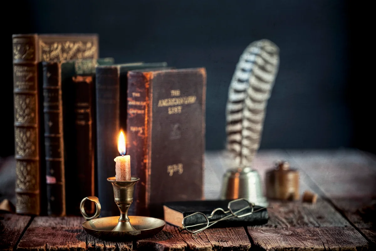 Study area with old books, quill pen and antique candle holder on an old wood desk