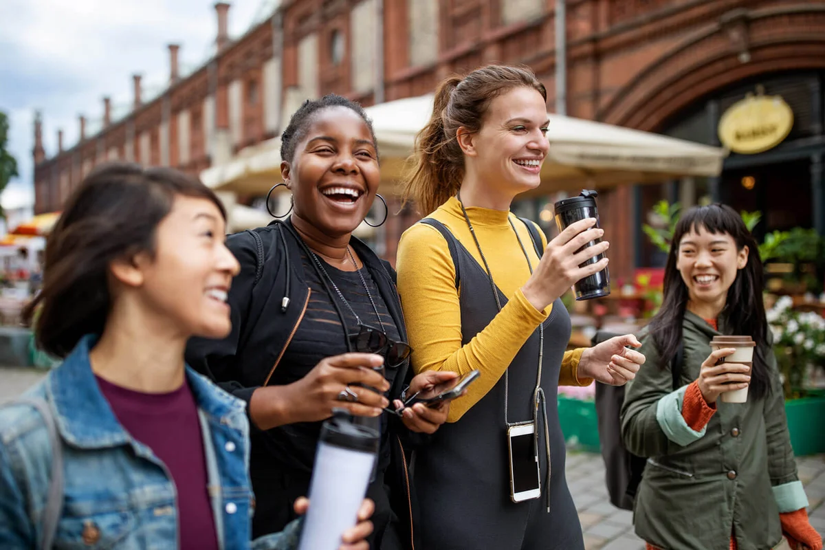 Happy female friends with drinks walking in city
