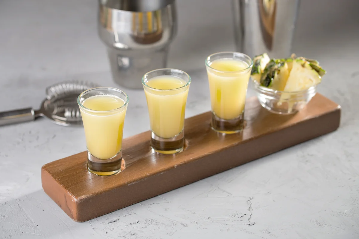 Shot glasses with pineapple slices on wooden board