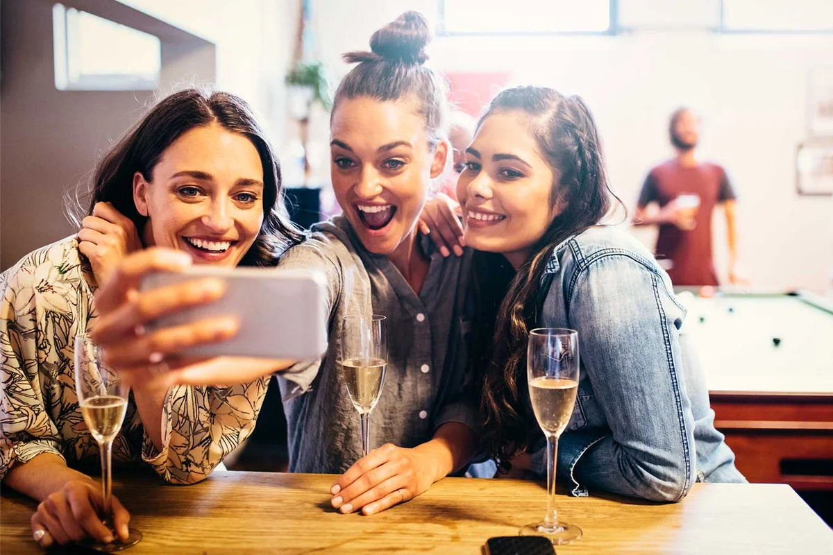 girlfriends at a bar drinking cocktails and taking selfie