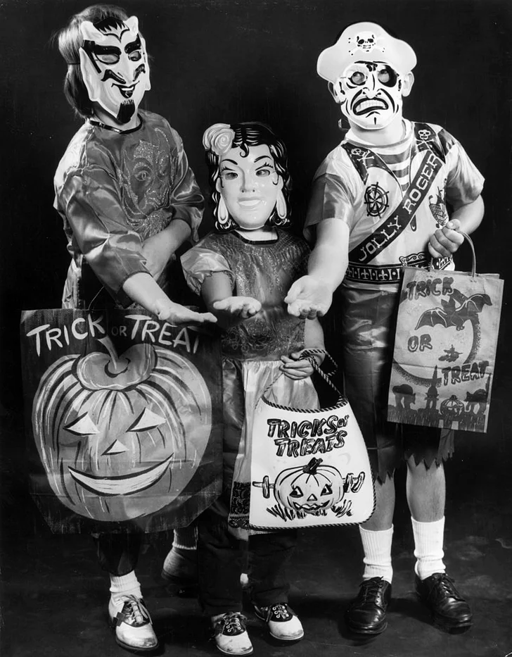 Three children wearing Halloween costumes and holding trick-or-treat bags
