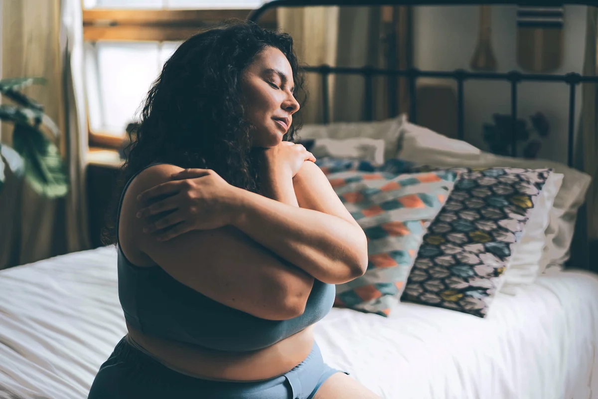 Woman in blue top and shorts with satisfaction on face hugs herself