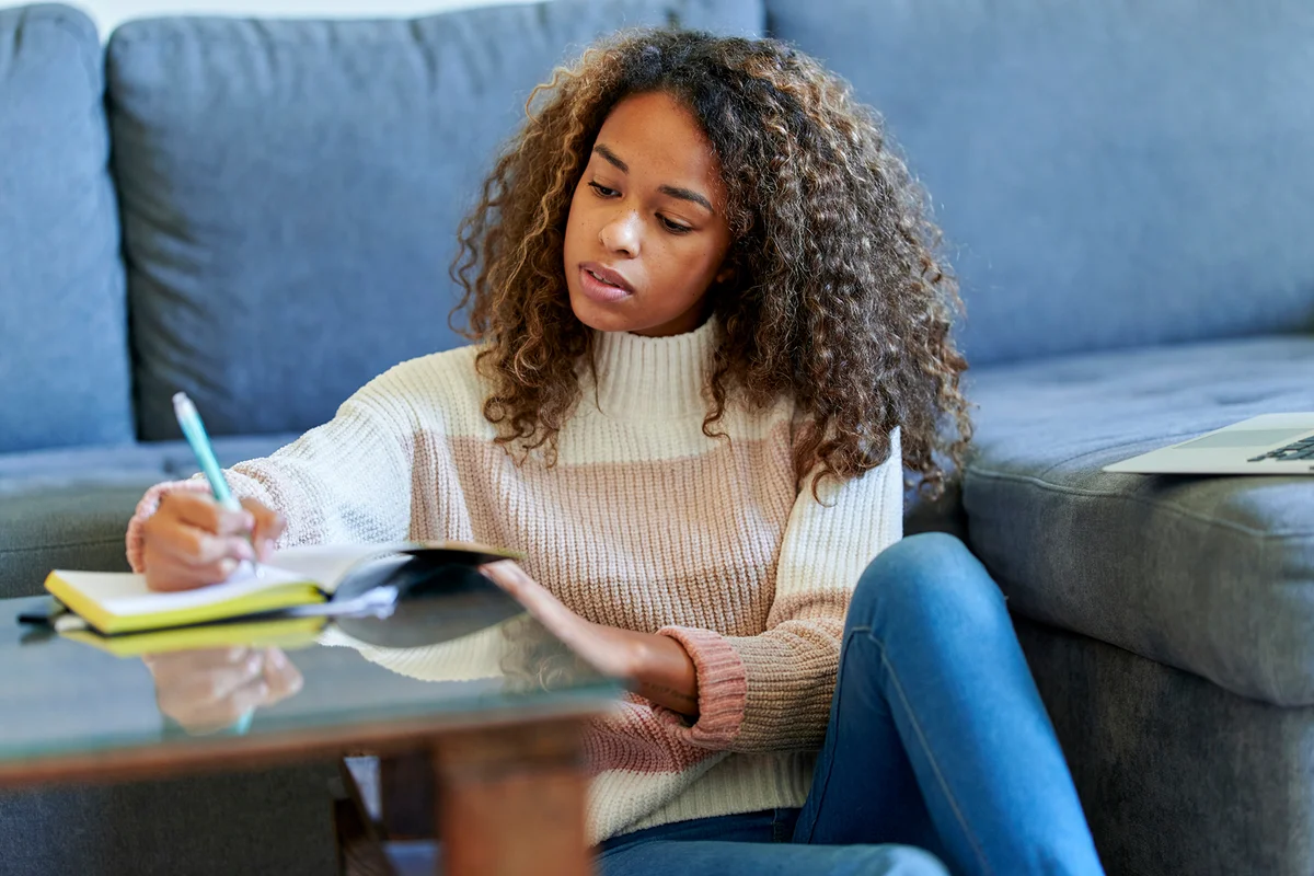 young woman with laptop writing in notepad at home