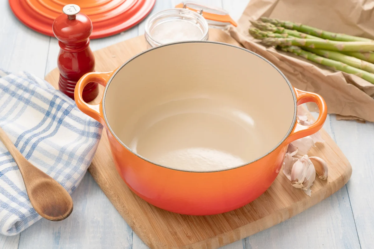 Orange dutch oven on wooden board with ingredients around it