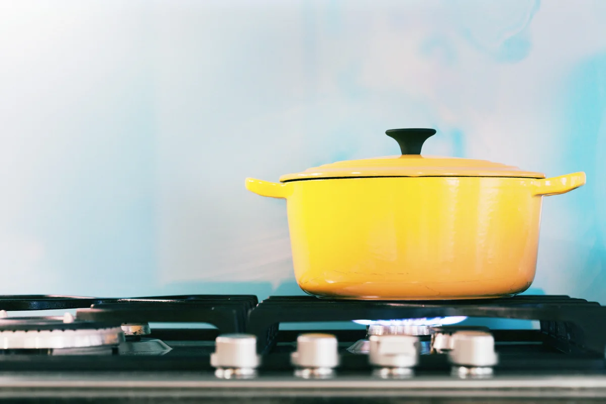 Yellow enamel casserole is cooking something on a gas stove