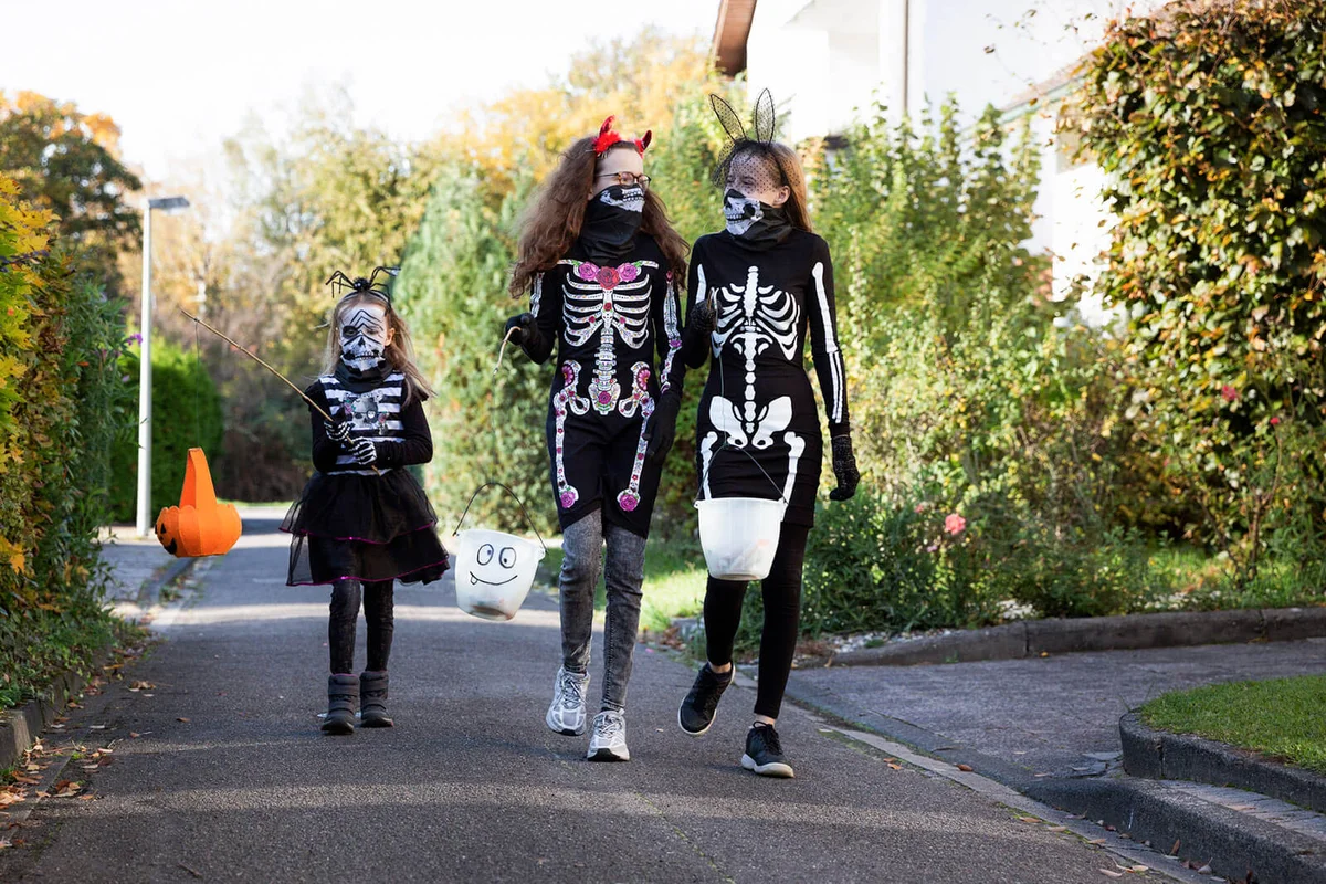 Child and teenagers walking along a narrow urban street whilst out trick or treating for Halloween
