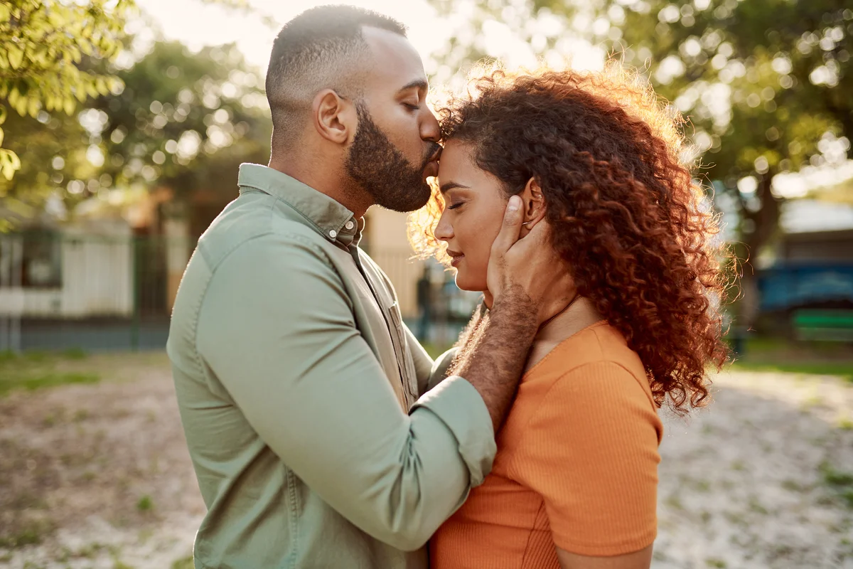 Young man giving his girlfriend a kiss on the forehead outdoors