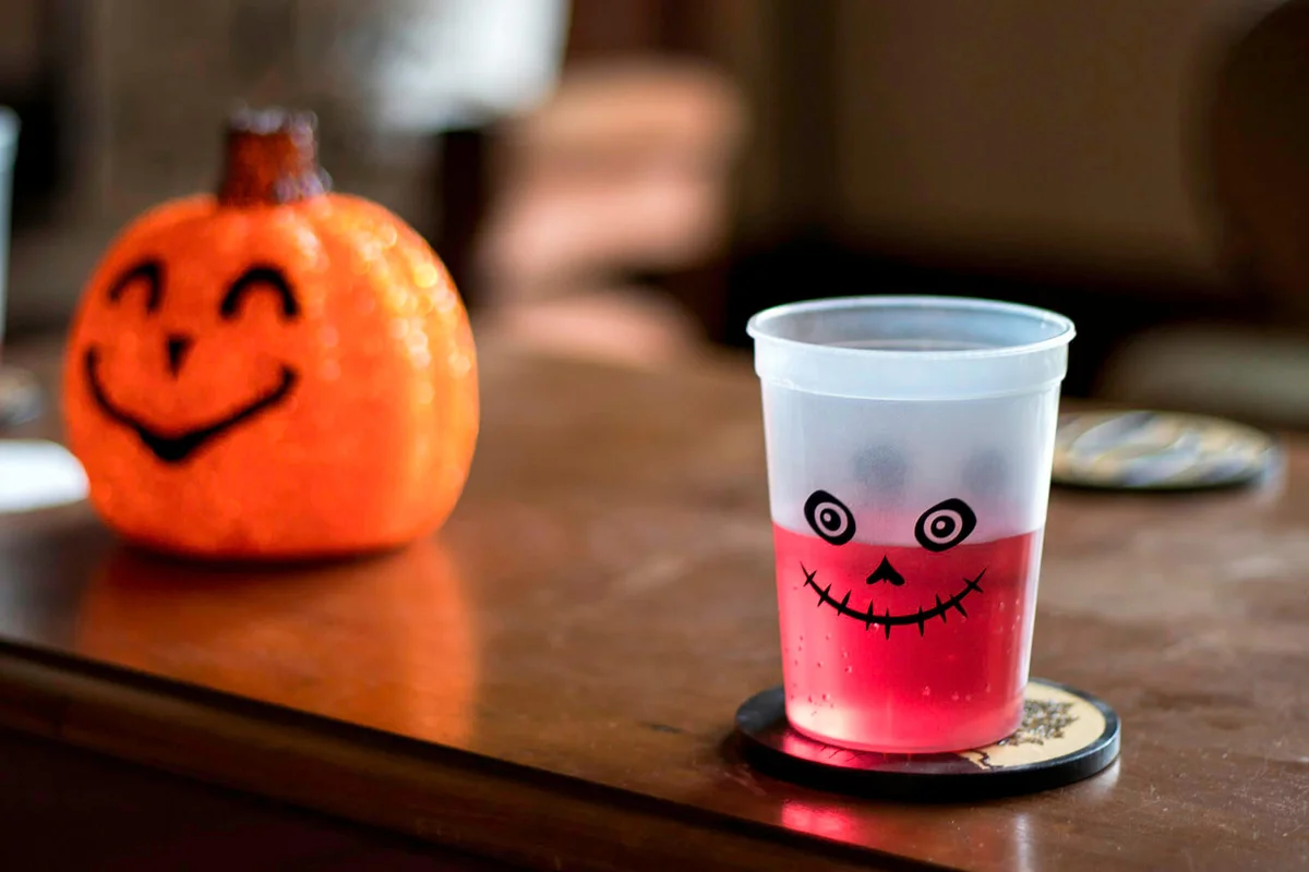 Red Halloween drink in cup on table with pumpkin