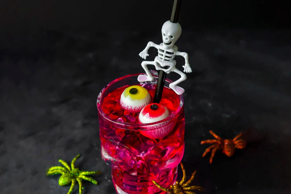 Red Halloween drink in skull cup with eyeballs floating and skeleton drinking straw