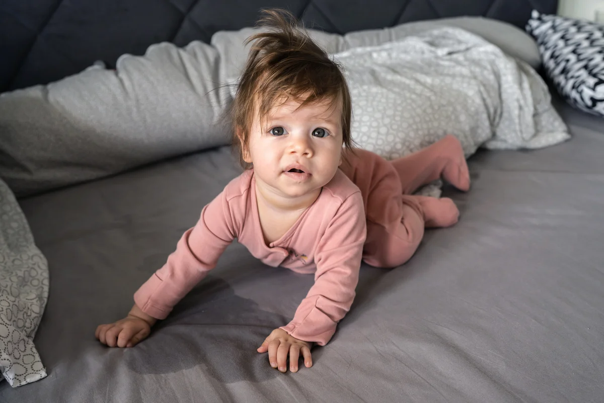 Baby on the bed with wet urine stain on the sheet