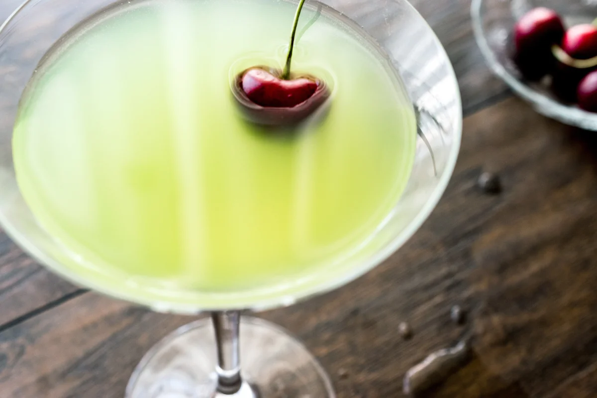 Green cocktail with cherry on wooden surface