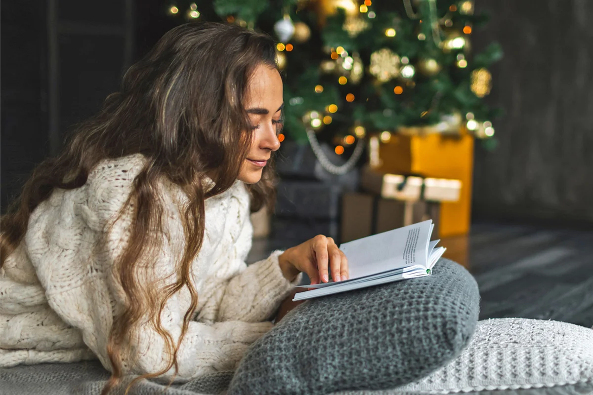 woman reading book by Christmas tree