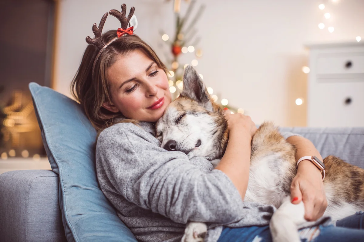 Women sitting on couch wearing christmas mask and holding her dog