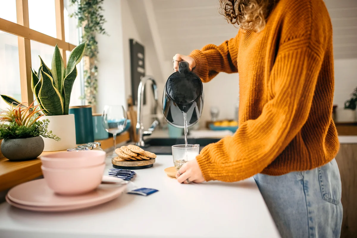 Young woman making tea with an electric kettle in her kitchen