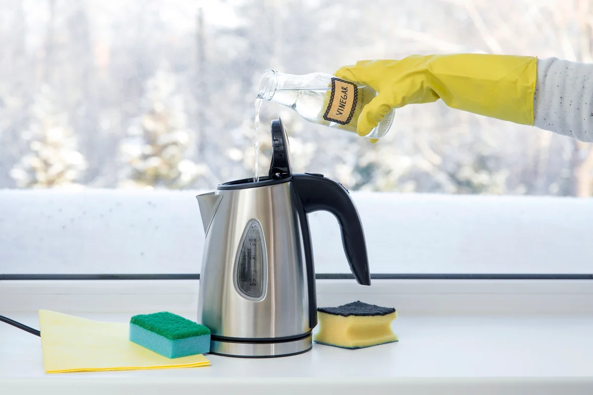 Woman pouring natural distilled acid white vinegar in electric kettle