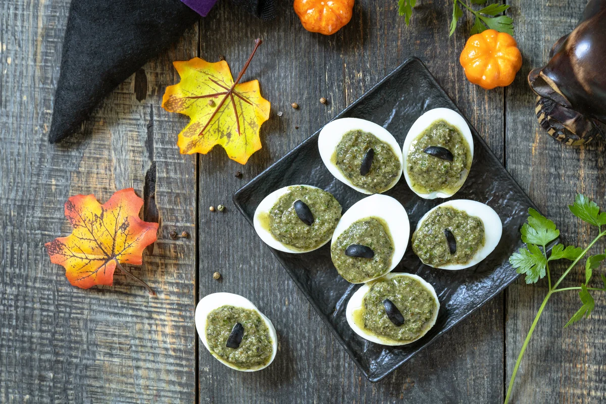 Halloween creative stuffed eggs with pesto sauce on a wooden table