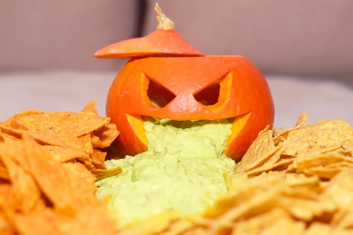 Carved pumpkin filled with guacamole and tortilla chips