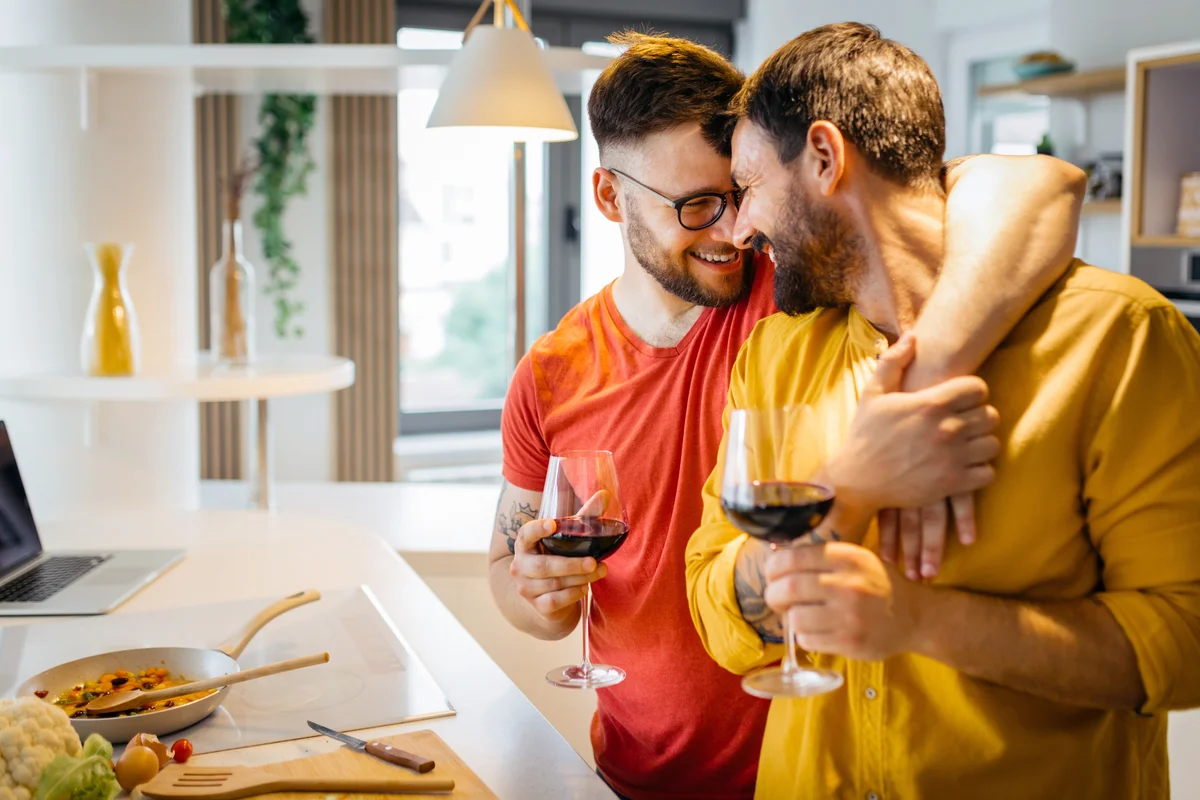 Gay couple hugging while cooking dinner together and drinking wine