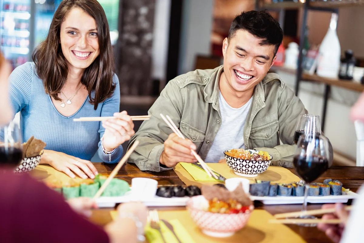 Friends laughing while eating asian food and drinking wine