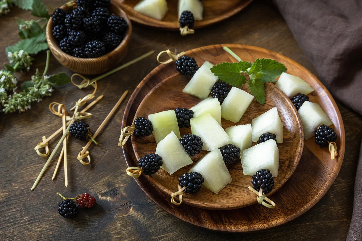 Canapes with melon and blackberries on a wooden table.