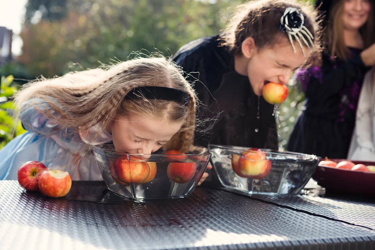 Two older children playing Halloween bobbing for apples game
