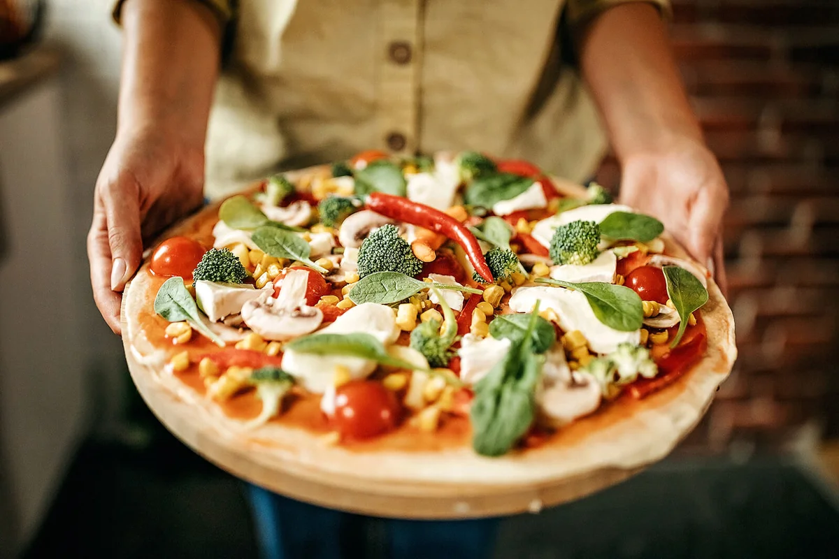 Women holding homemade pizza, preparing for cooking