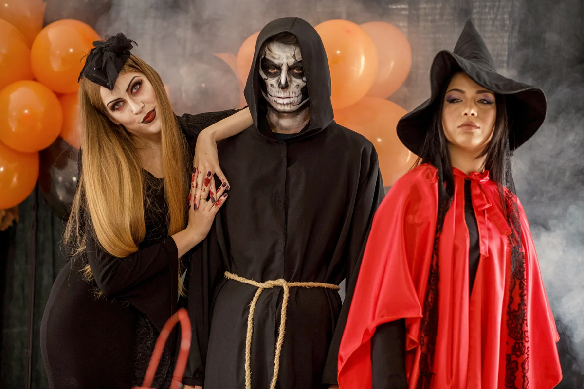 Three people posing in a vampire, grim reader and witch costumes for Halloween