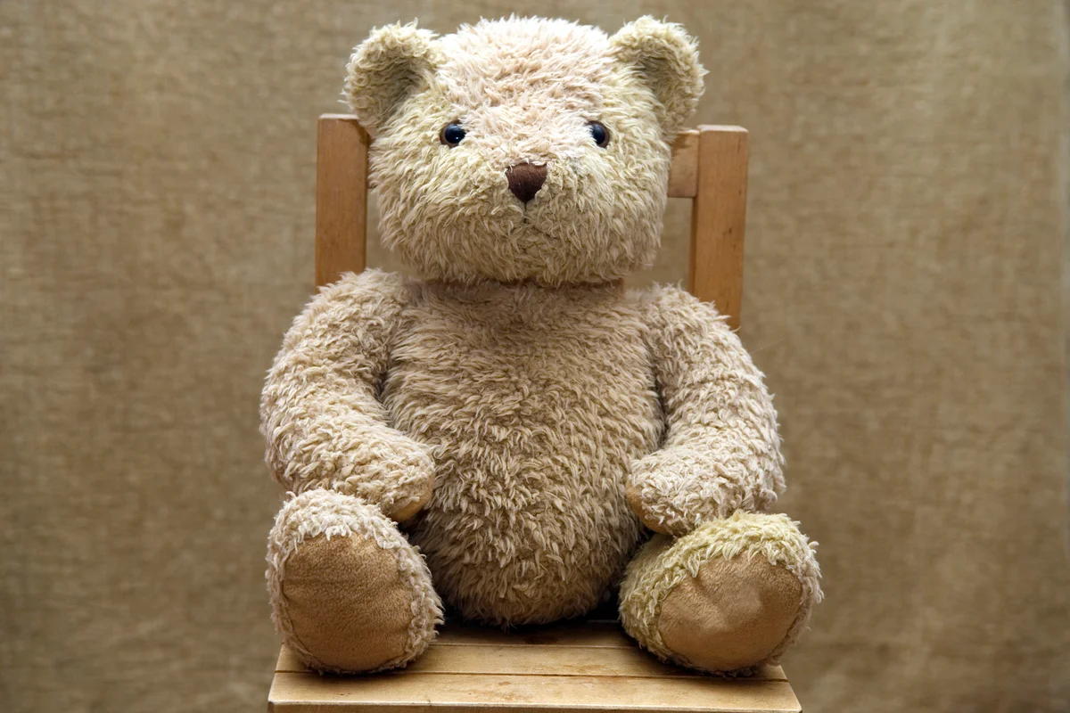 Old teddy bear sitting on wooden chair