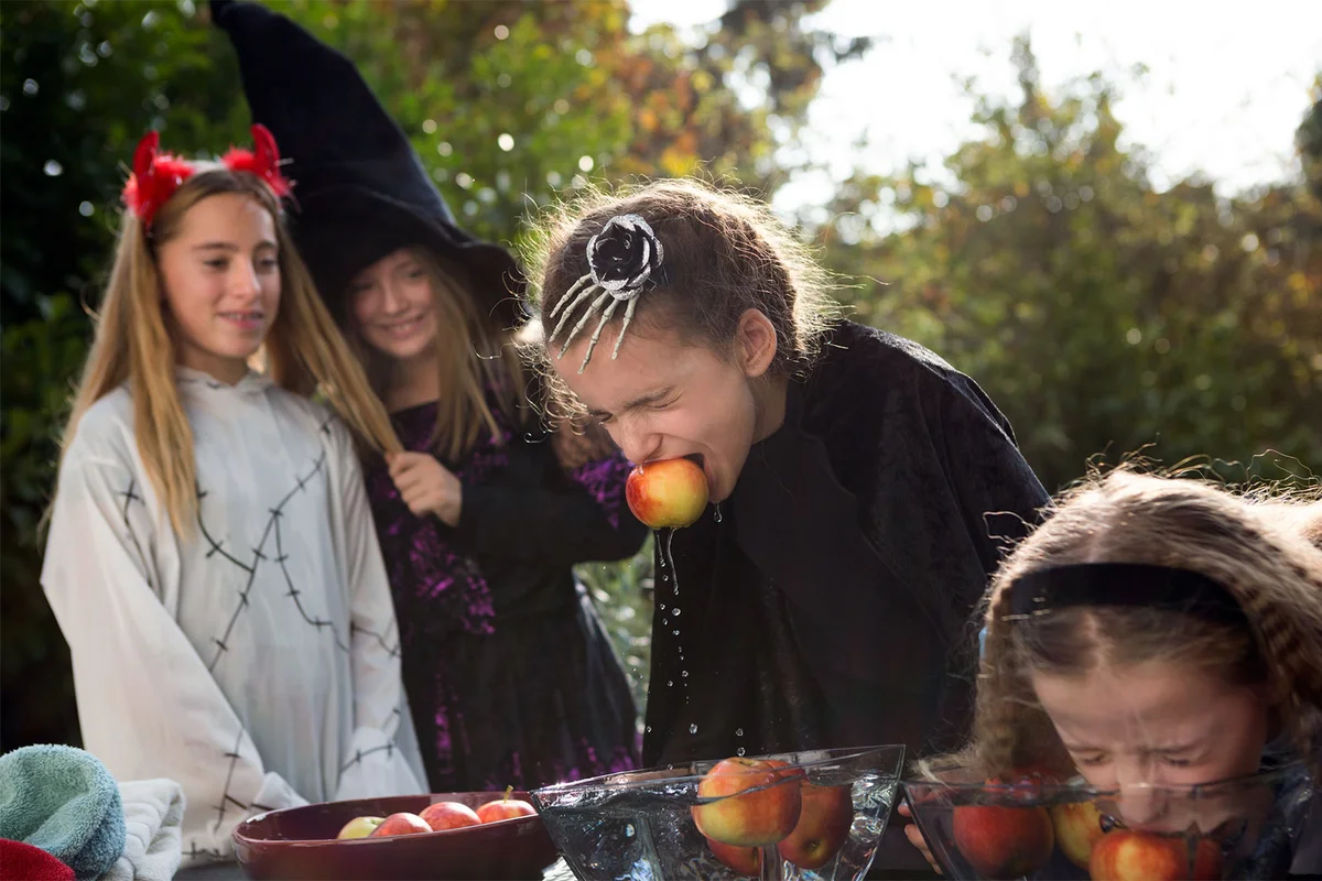 Children in costumes bobbing for apples on Halloween