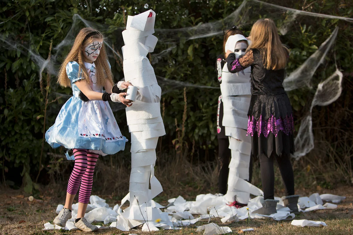 Children playing Halloween party game Wrap the Mummy