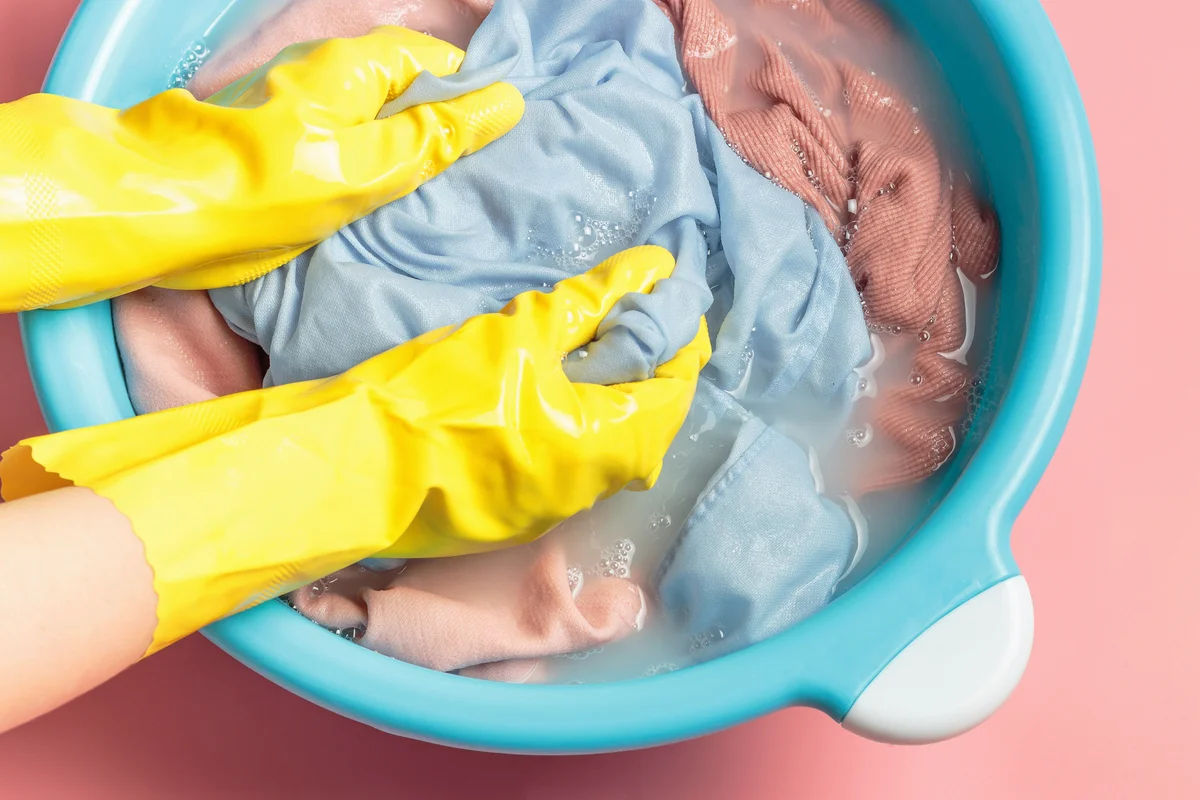 Female hands in rubber gloves washing pink clothes in basin