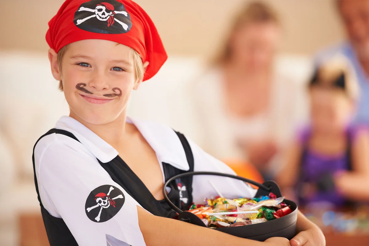 child in pirate costume holding bucket of candy to pass out